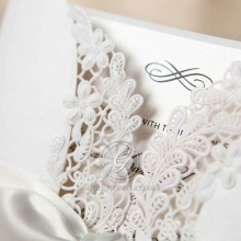 Elegant symbol in raised ink printing, ivory insert card, enclosed in a white gatefold invite with floral lasercut design with ribbon