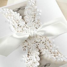 Intricate lasercut details on a white gatefold sleeve, bound by a satin lace tied in a knot, insert card with raised ink printing 