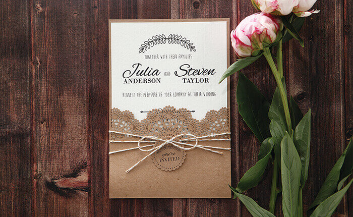 A rustic laser cut pocket invite with textured inner card and yarn beside blooms 