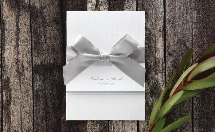 An elegant white wedding invite with a silky silver ribbon and foiled flap