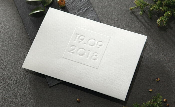A textured white wedding invite tri-fold with an embossed date in the center